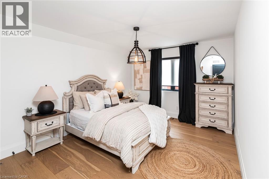 Hardwood-style flooring extends throughout this room, featuring a window with dark draperies, white baseboards, and a contemporary ceiling light fixture - 253 Central Avenue, Grimsby, ON