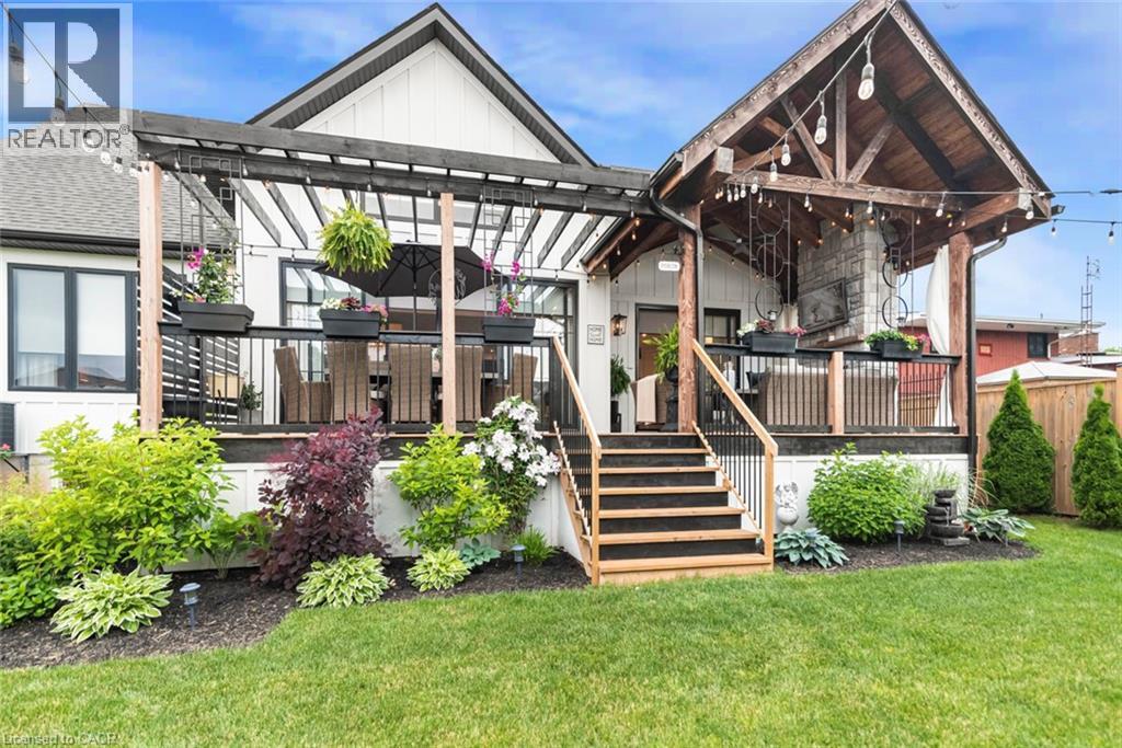 Expansive backyard featuring a manicured lawn, multi-level deck with black railing, and mature landscaping - 253 Central Avenue, Grimsby, ON