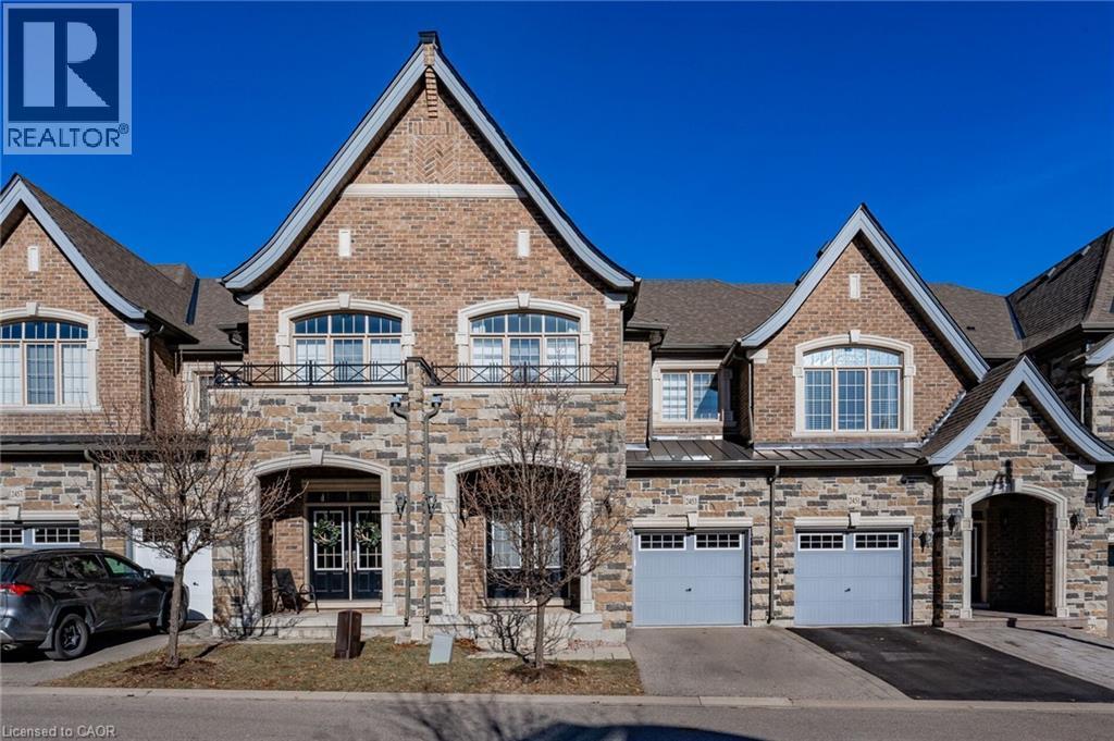 The property features an appealing exterior facade with a combination of brick and stone, a prominent front entrance, and two distinct garage doors - 2453 Village Common, Oakville, ON - Outdoor With Facade