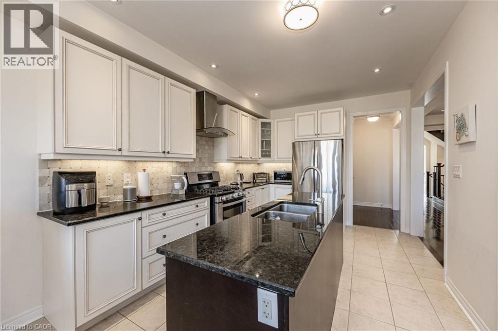 The kitchen features white cabinetry, dark countertops, a stainless steel refrigerator, and a kitchen island with an integrated sink - 2453 Village Common, Oakville, ON - Indoor Photo Showing Kitchen With Stainless Steel Kitchen With Double Sink With Upgraded Kitchen
