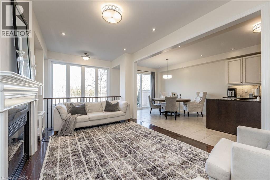 This open-concept living area features hardwood flooring, a fireplace with a white mantel, and large windows providing natural light - 2453 Village Common, Oakville, ON - Indoor Photo Showing Living Room With Fireplace