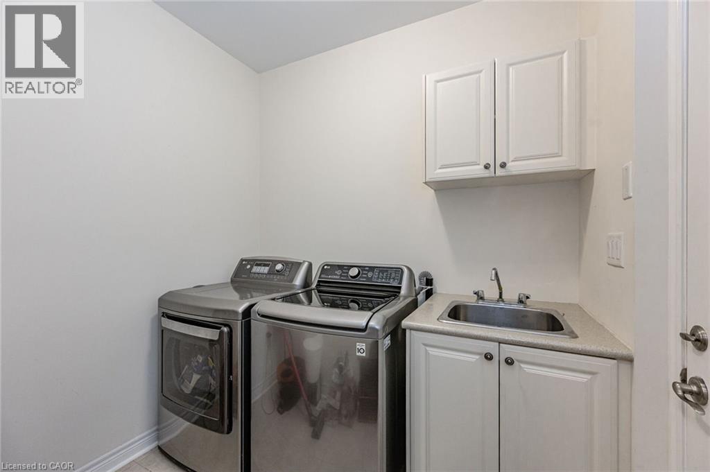 Laundry room featuring a stainless steel washer and dryer, a utility sink with a countertop, and white cabinetry - 2453 Village Common, Oakville, ON - Indoor Photo Showing Laundry Room