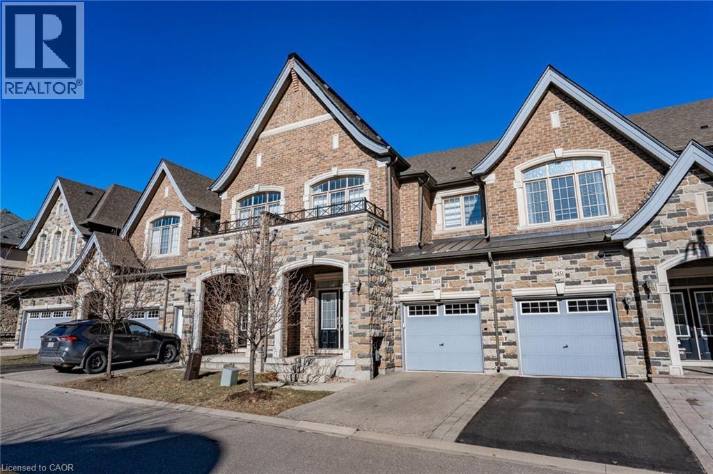 The property features an appealing brick and stone facade, arched entryway, and a balcony with a wrought iron railing - 2453 Village Common, Oakville, ON - Outdoor With Facade