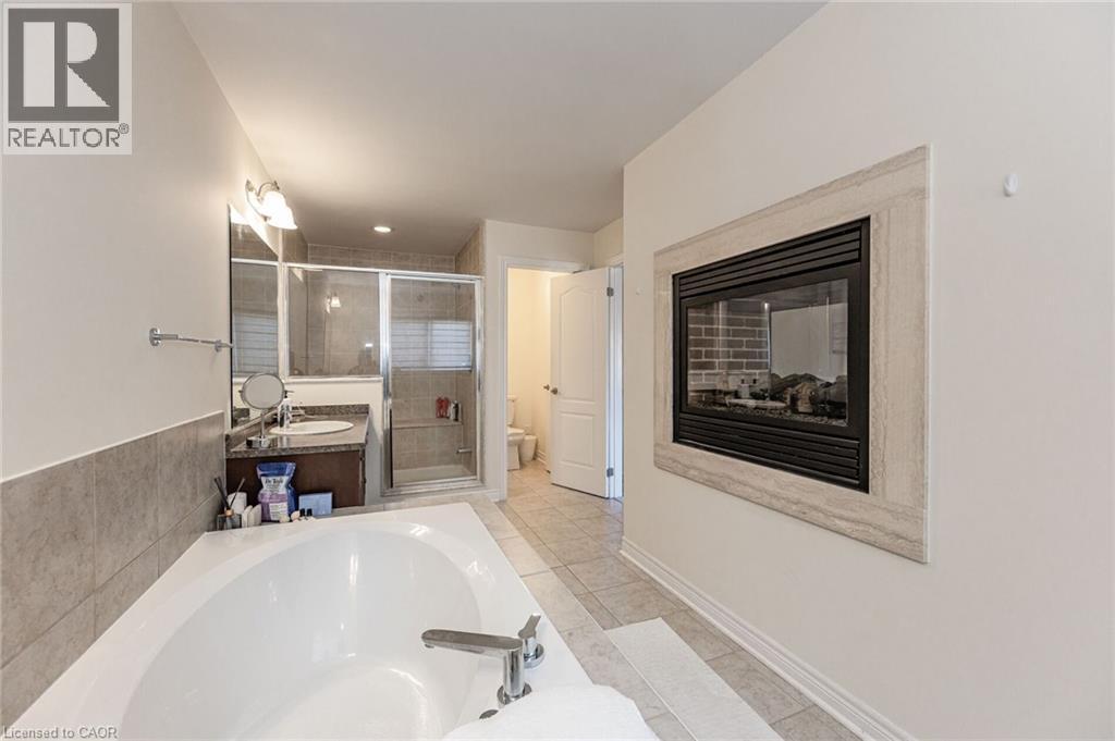 Bathroom featuring a built-in fireplace, a white soaking tub with a chrome faucet, a vanity with a sink and mirror, and a glass-enclosed shower - 2453 Village Common, Oakville, ON - Indoor Photo Showing Bathroom