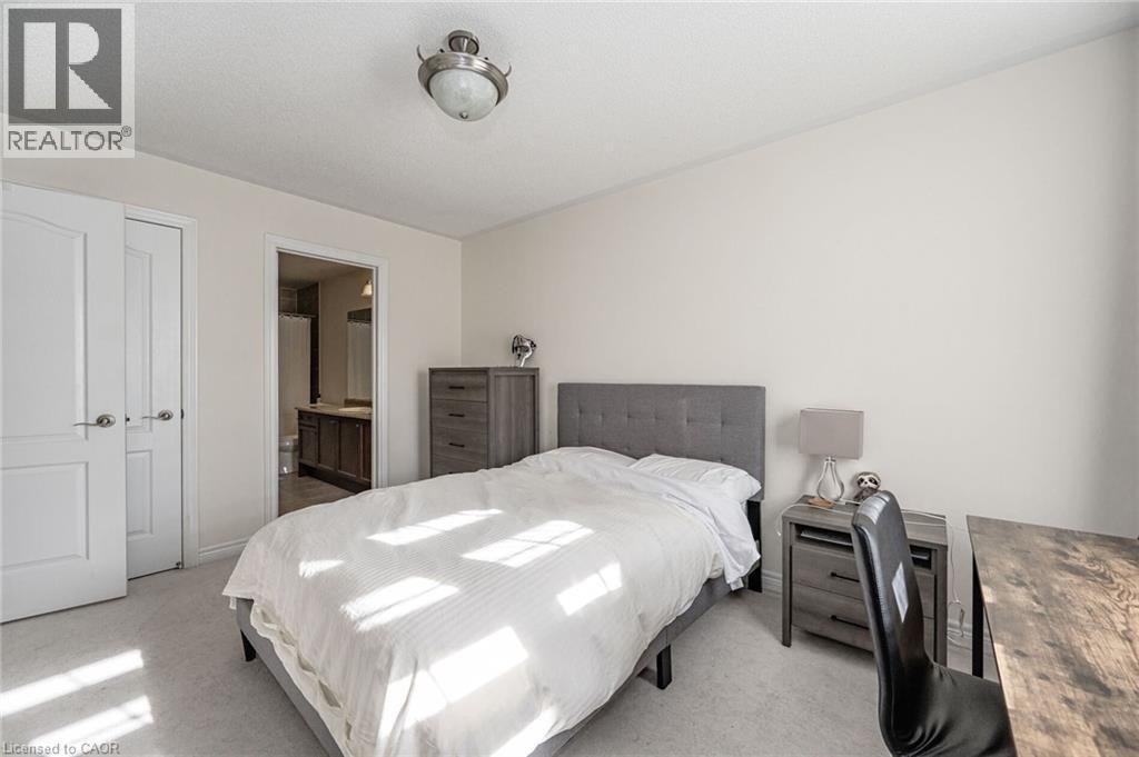 This room features light-colored walls and carpeting, a bed with a gray upholstered headboard, and a ceiling-mounted light fixture - 2453 Village Common, Oakville, ON - Indoor Photo Showing Bedroom