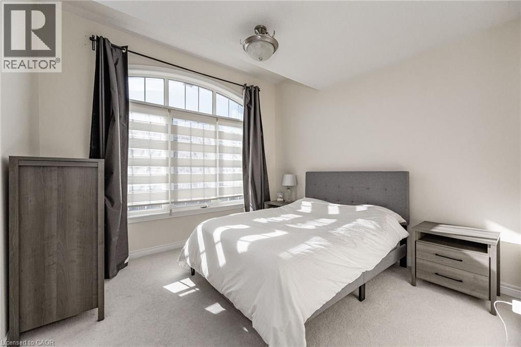 This room features a large arched window with blinds and dark curtains, light-colored walls, and carpeting - 2453 Village Common, Oakville, ON - Indoor Photo Showing Bedroom