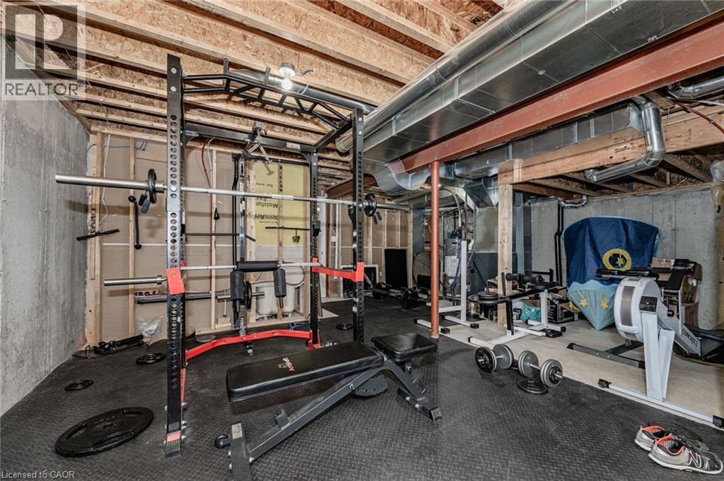 The basement features exposed wooden ceiling beams and concrete walls, with a portion of the floor covered in black rubber matting - 2453 Village Common, Oakville, ON - Indoor Photo Showing Gym Room