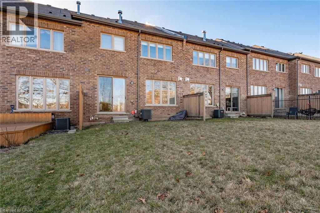 The property features a brick exterior with a well-maintained lawn and a wooden deck - 2453 Village Common, Oakville, ON - Outdoor With Exterior