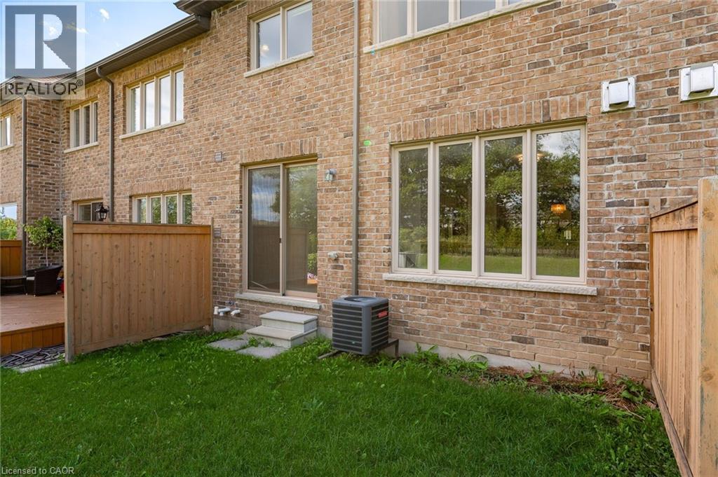 The property features a brick exterior, a well-maintained lawn, and a wooden fence - 2453 Village Common, Oakville, ON - Outdoor With Exterior