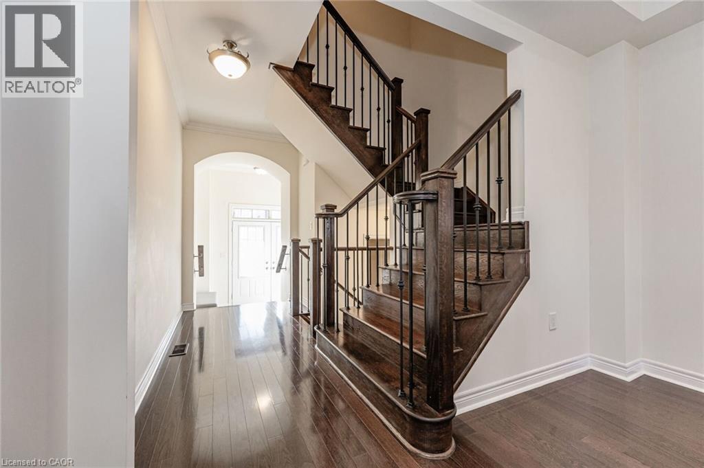 The property features rich hardwood floors, an elegant staircase with dark wood and wrought iron balusters, and an arched entryway - 2453 Village Common, Oakville, ON - Indoor Photo Showing Other Room