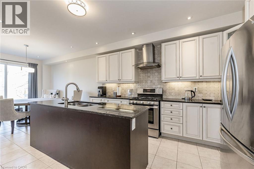 The kitchen features white cabinetry, black countertops, and stainless steel appliances, including a range and refrigerator - 2453 Village Common, Oakville, ON - Indoor Photo Showing Kitchen With Stainless Steel Kitchen With Double Sink With Upgraded Kitchen