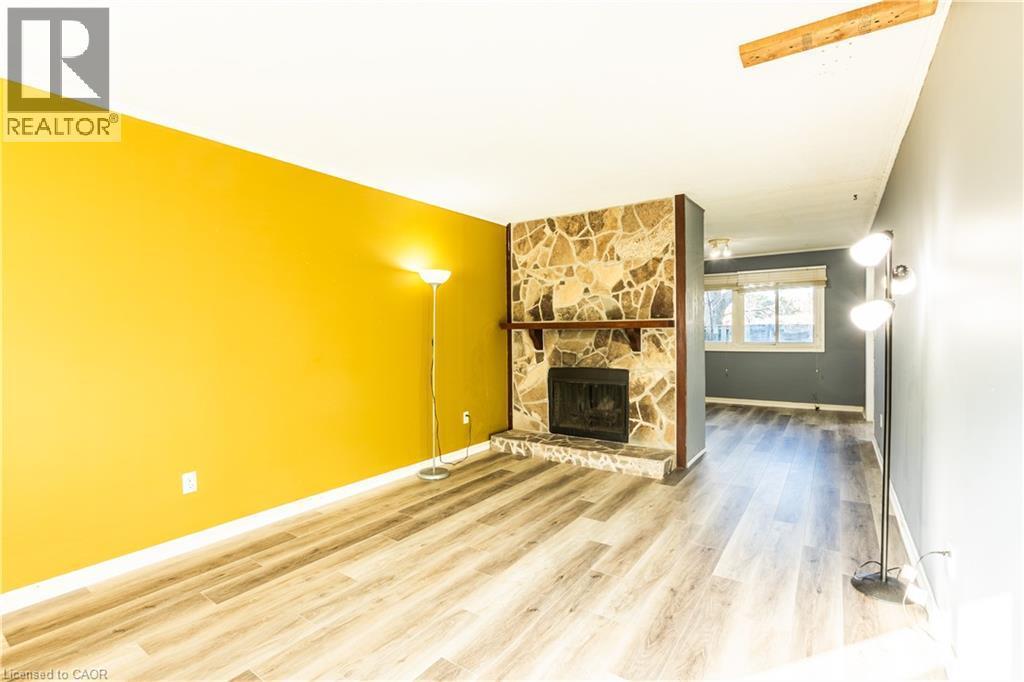 The living area features light wood-style flooring, a stone fireplace with a wooden mantel, and a bright yellow accent wall - 121 University Avenue E Unit# 102, Waterloo, ON - Indoor With Fireplace