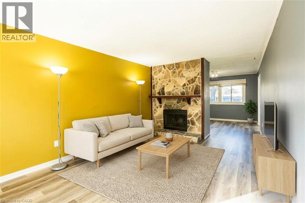 Living area featuring a stone fireplace, wood-look flooring, and a window providing natural light - 121 University Avenue E Unit# 102, Waterloo, ON - Indoor Photo Showing Living Room With Fireplace