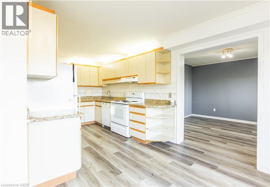 The kitchen features white cabinetry, granite-style countertops, white appliances, and wood-look flooring - 121 University Avenue E Unit# 102, Waterloo, ON - Indoor Photo Showing Kitchen