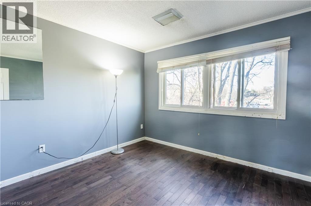 This room features dark hardwood flooring, light blue walls, and a large window with blinds that provides natural illumination - 121 University Avenue E Unit# 102, Waterloo, ON - Indoor Photo Showing Other Room