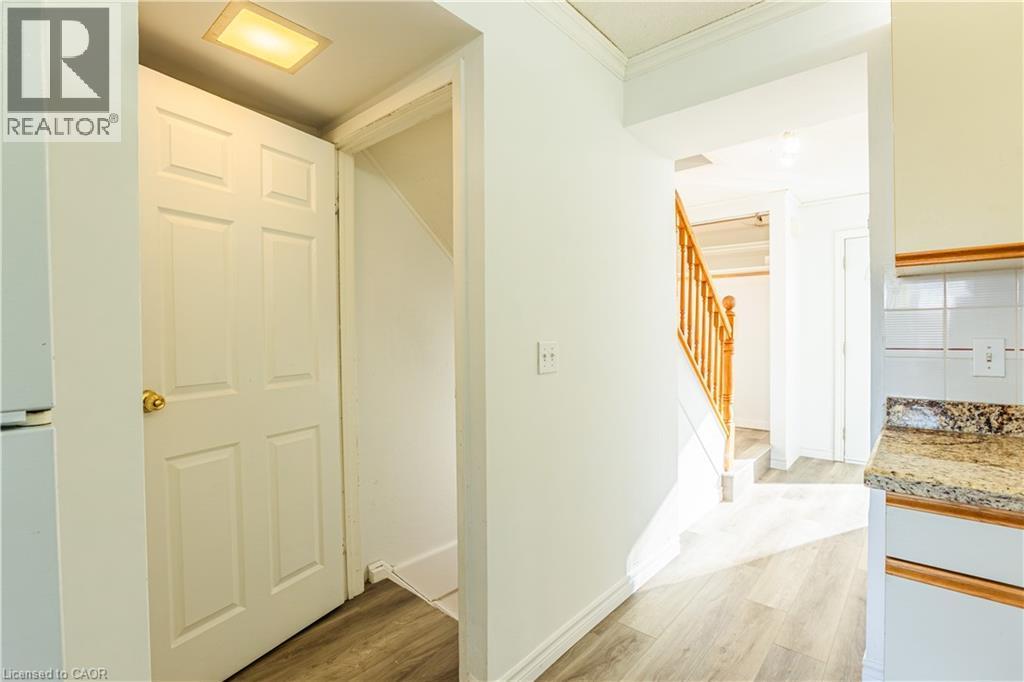 The property features a staircase with a wooden railing, light-colored flooring, and a kitchen area with white cabinetry, a tiled backsplash, and a granite-patterned countertop - 121 University Avenue E Unit# 102, Waterloo, ON - Indoor Photo Showing Other Room