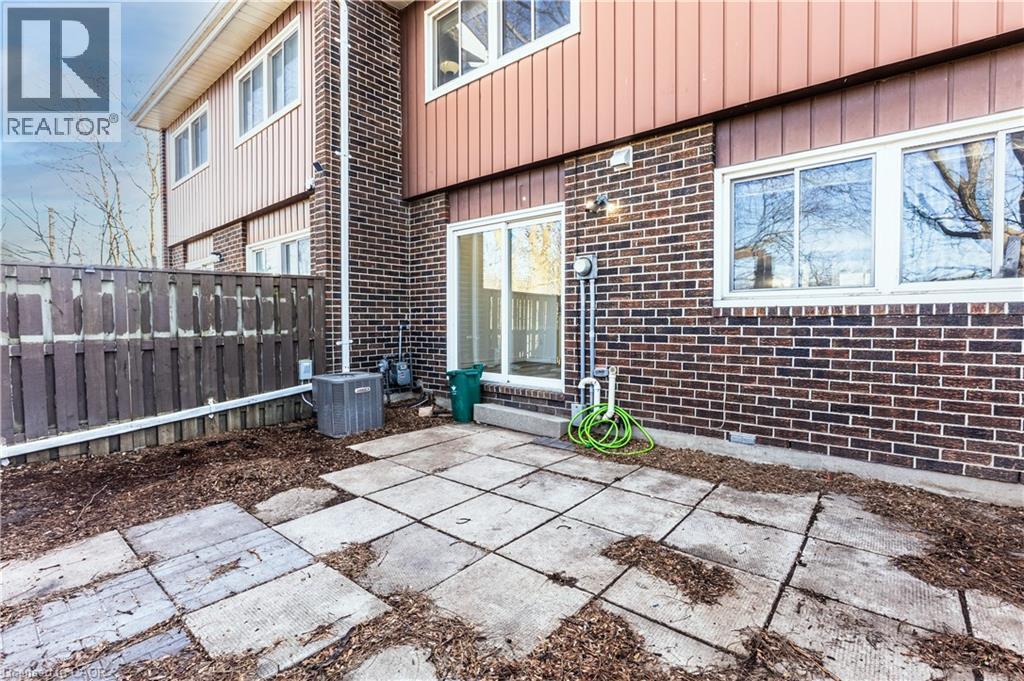 The property features a patio with square concrete pavers, a privacy fence, and a brick exterior with white-framed windows - 121 University Avenue E Unit# 102, Waterloo, ON - Outdoor