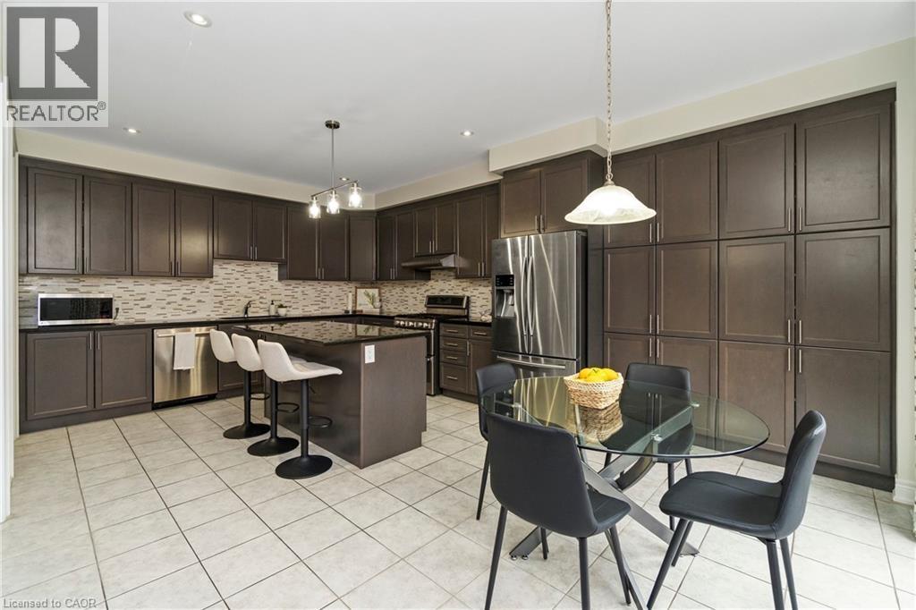 The kitchen features extensive dark cabinetry, a kitchen island with seating, stainless steel appliances, and tiled flooring - 4 Macbean Crescent, Waterdown, ON - Indoor