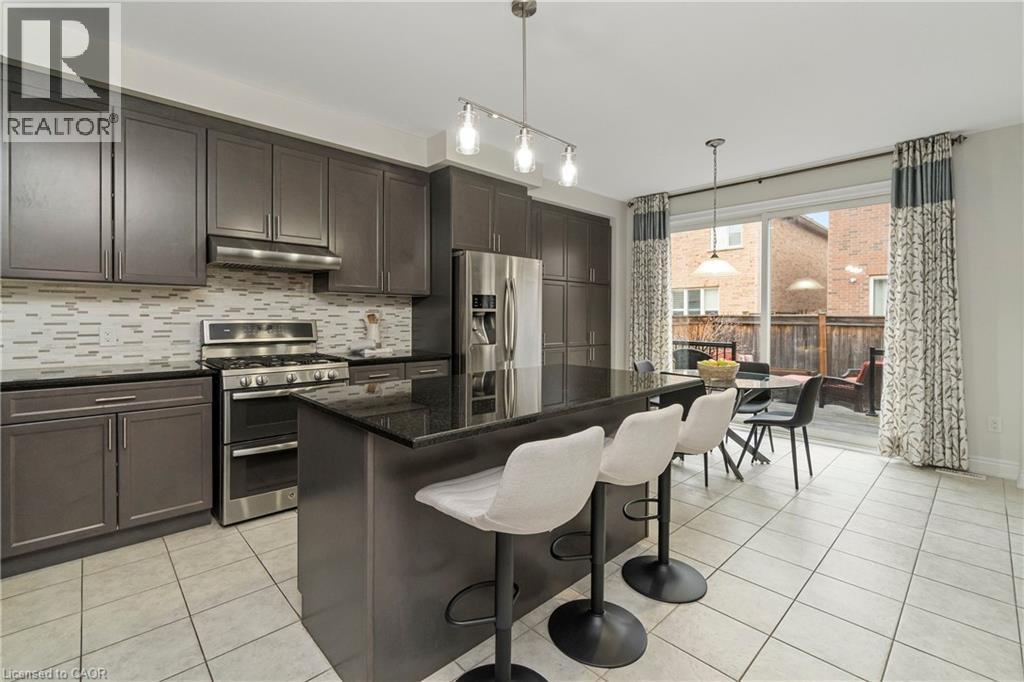The kitchen features dark cabinetry, stainless steel appliances, a center island with bar seating, and a tile backsplash - 4 Macbean Crescent, Waterdown, ON - Indoor Photo Showing Kitchen With Upgraded Kitchen