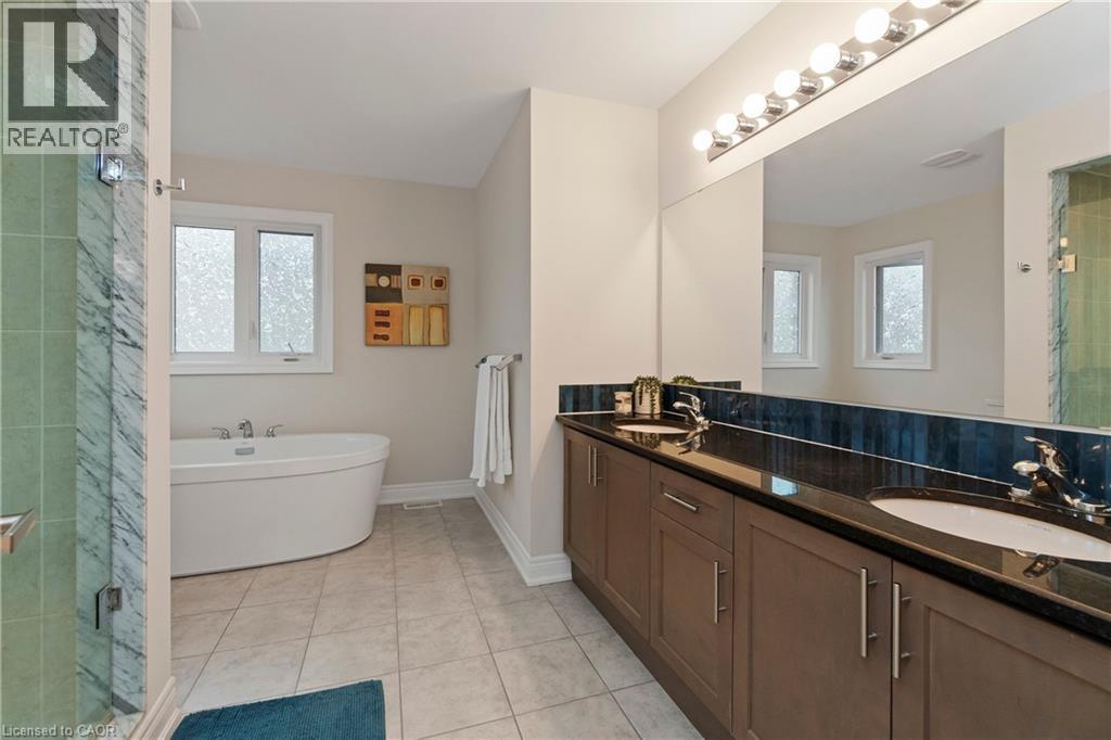 The bathroom features a double vanity with dark countertops and integrated sinks, a large mirror with overhead lighting, a freestanding bathtub beneath a window, and a shower enclosure with glass and - 4 Macbean Crescent, Waterdown, ON - Indoor Photo Showing Bathroom