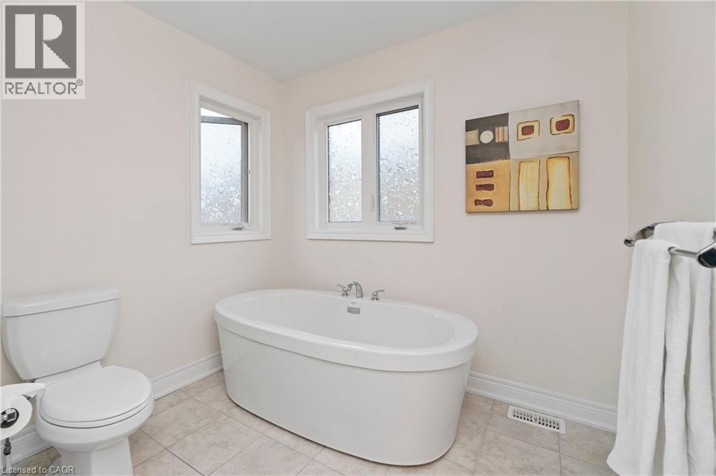 Spacious bathroom featuring a freestanding oval bathtub, a toilet, and two windows - 4 Macbean Crescent, Waterdown, ON - Indoor Photo Showing Bathroom