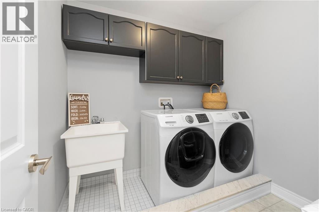 Laundry area featuring a utility sink, dark cabinetry, and white tile flooring - 4 Macbean Crescent, Waterdown, ON - Indoor Photo Showing Laundry Room