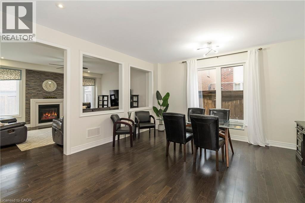 The dining area features dark hardwood flooring, a window with white curtains, and a ceiling light fixture - 4 Macbean Crescent, Waterdown, ON - Indoor With Fireplace