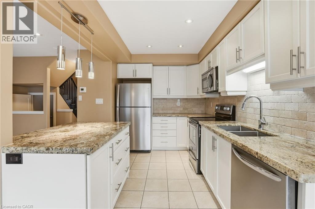 Kitchen with stainless steel appliances, light stone countertops, white cabinets, light tile patterned floors, and hanging light fixtures - 91 Chamomile Drive, Hamilton, ON - Indoor Photo Showing Kitchen With Stainless Steel Kitchen With Double Sink With Upgraded Kitchen
