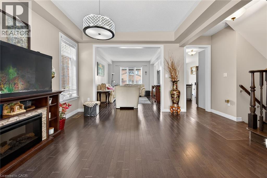 The property features dark hardwood flooring throughout, a decorative light fixture, and an open concept layout providing clear sightlines to other areas - 44 Matteo Trail, Hamilton, ON - Indoor Photo Showing Living Room With Fireplace
