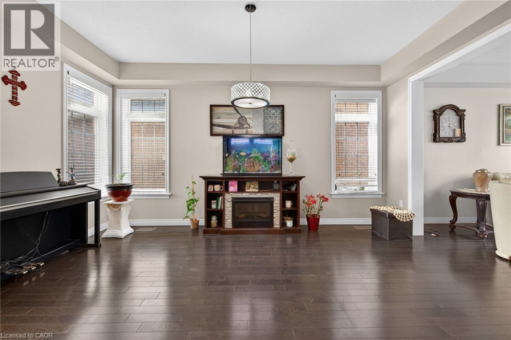 The living area features dark hardwood flooring, light-colored walls, and large windows with blinds - 44 Matteo Trail, Hamilton, ON - Indoor Photo Showing Other Room