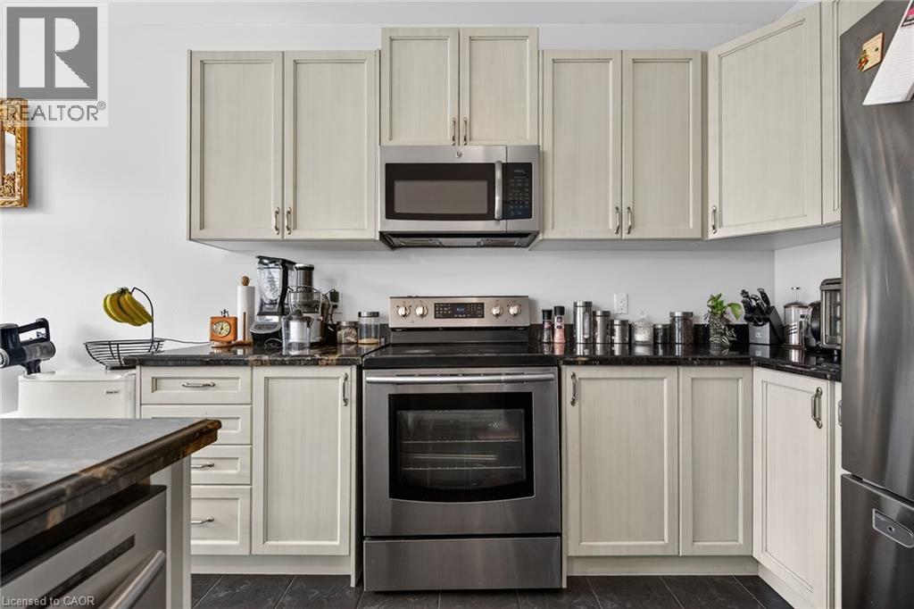 The kitchen features light-colored cabinetry, dark countertops, a stainless steel range, and a matching microwave - 44 Matteo Trail, Hamilton, ON - Indoor Photo Showing Kitchen