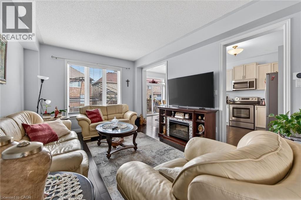 Living room featuring dark wood flooring, a decorative rug, and a large window with blinds - 44 Matteo Trail, Hamilton, ON - Indoor Photo Showing Living Room