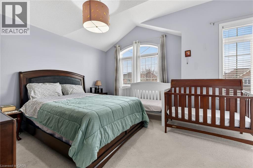 This room features a vaulted ceiling, a bed with a dark wood frame, and arched windows with horizontal blinds - 44 Matteo Trail, Hamilton, ON - Indoor Photo Showing Bedroom