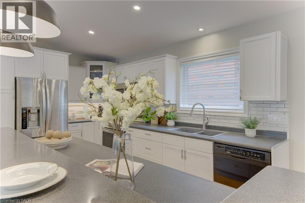 The kitchen features a double basin stainless steel sink, a stainless steel refrigerator, a black dishwasher, and white cabinetry - 400 Manchester Road, Kitchener, ON - Indoor Photo Showing Kitchen With Double Sink