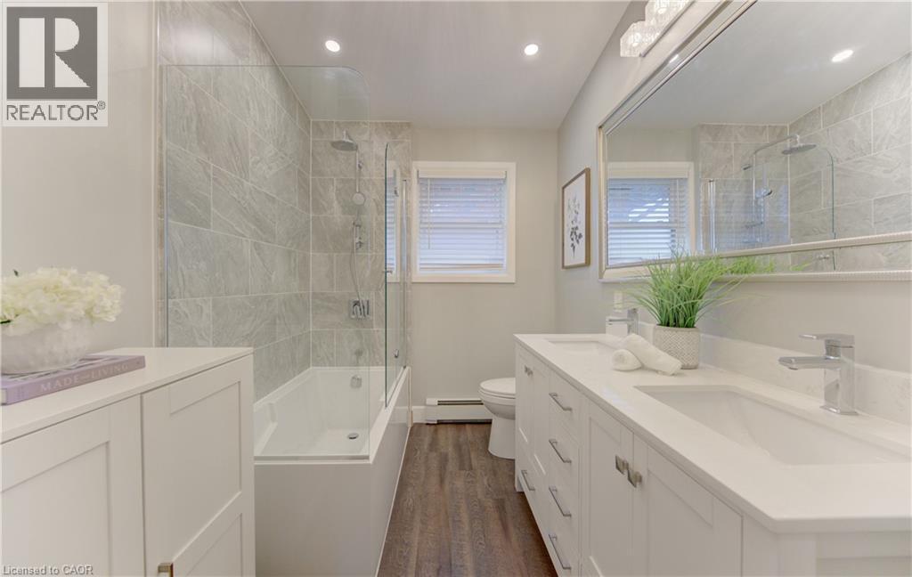 Bathroom featuring a double vanity with white cabinets and a white countertop, a large mirror, a bathtub with a glass shower screen, and tiled walls in the shower area - 400 Manchester Road, Kitchener, ON - Indoor Photo Showing Bathroom