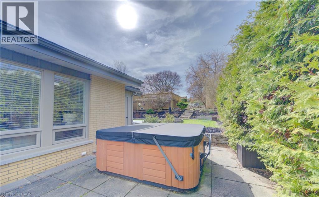 The property features a private patio with a hot tub, bordered by lush green foliage - 400 Manchester Road, Kitchener, ON - Outdoor With Deck Patio Veranda