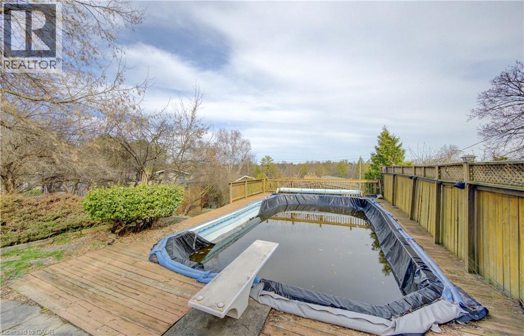 The property features an outdoor swimming pool with a diving board, surrounded by a wooden deck and a privacy fence - 400 Manchester Road, Kitchener, ON - Outdoor