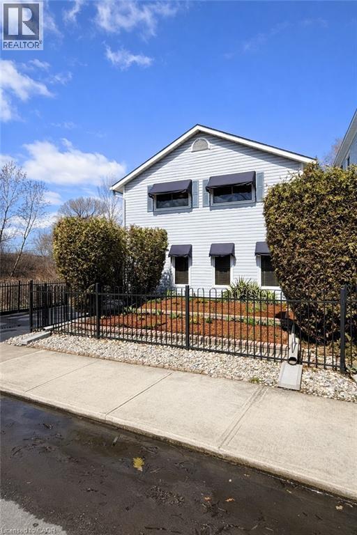 The property features light-colored siding, a gable roof, and dark window awnings - 21 Arden Avenue, Hamilton, ON