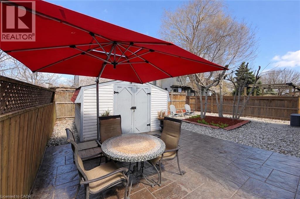 The property features a private outdoor area with stamped concrete patio, a red patio umbrella, and a storage shed - 21 Arden Avenue, Hamilton, ON