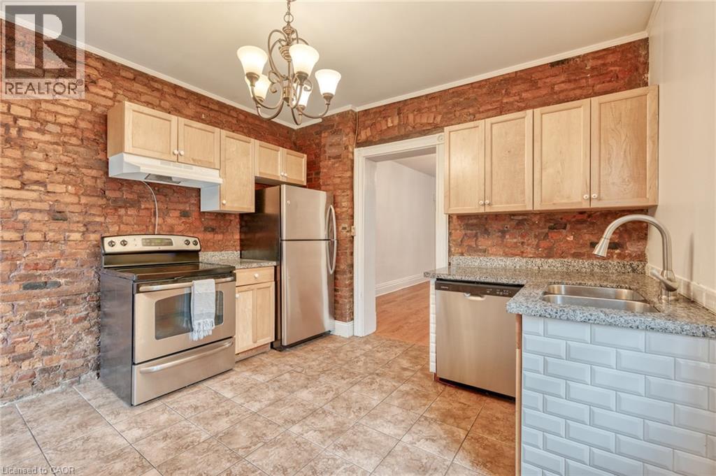 The kitchen features exposed brick walls, stainless steel appliances, tiled flooring, light wood cabinetry, and granite countertops - 198 Bay Street N, Hamilton, ON - Indoor Photo Showing Kitchen With Double Sink