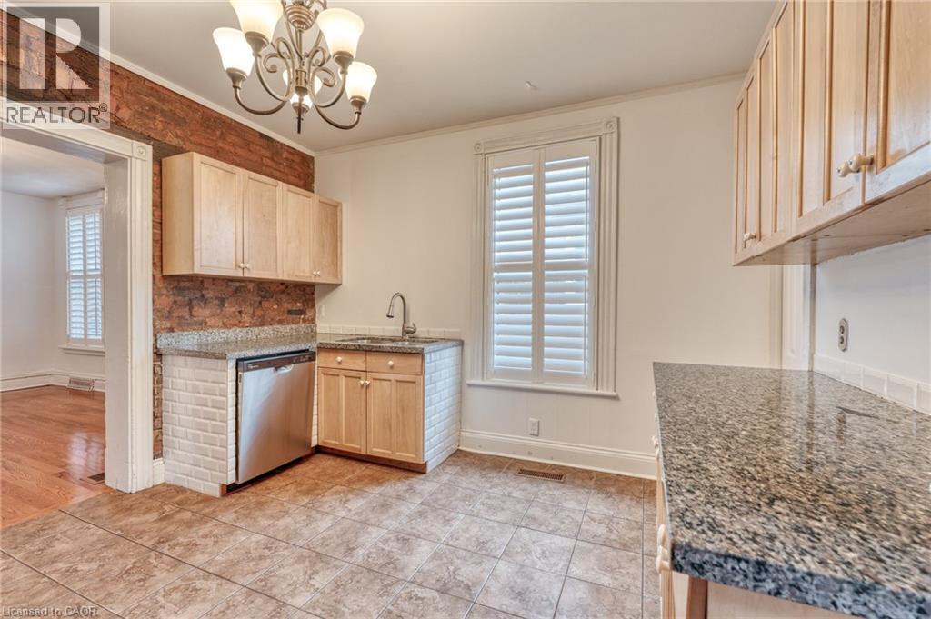 The kitchen features wood cabinetry, granite countertops, a stainless steel dishwasher, and a tile backsplash - 198 Bay Street N, Hamilton, ON - Indoor Photo Showing Kitchen