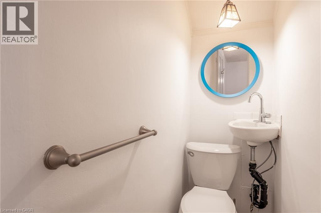 The bathroom features a toilet, a wall-mounted sink with a chrome faucet, a round mirror with a blue frame, and a bronze-toned towel bar - 198 Bay Street N, Hamilton, ON - Indoor Photo Showing Bathroom