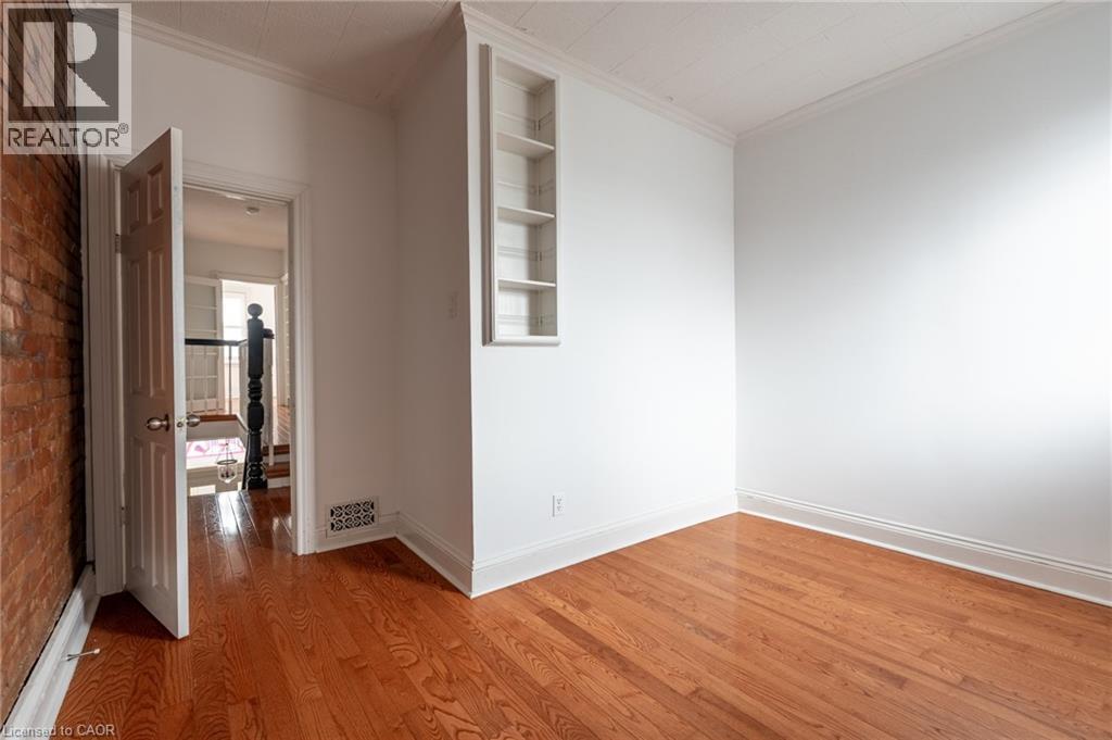 This room features hardwood floors, white walls, and an exposed brick wall - 198 Bay Street N, Hamilton, ON - Indoor Photo Showing Other Room