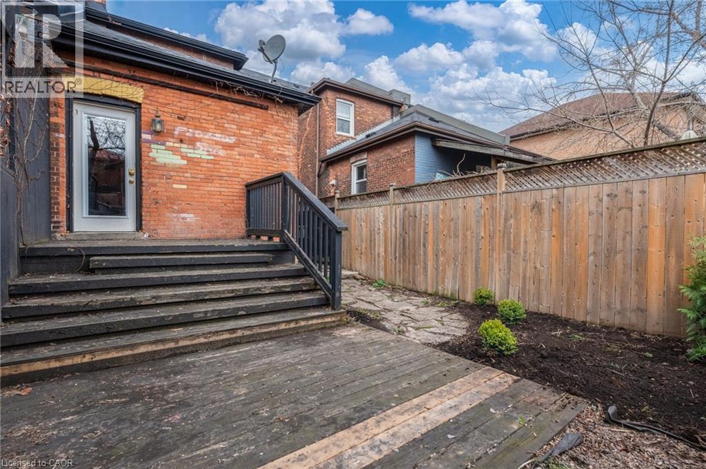 The property features a brick exterior with a rear entrance leading to a wooden deck and stairs - 198 Bay Street N, Hamilton, ON - Outdoor