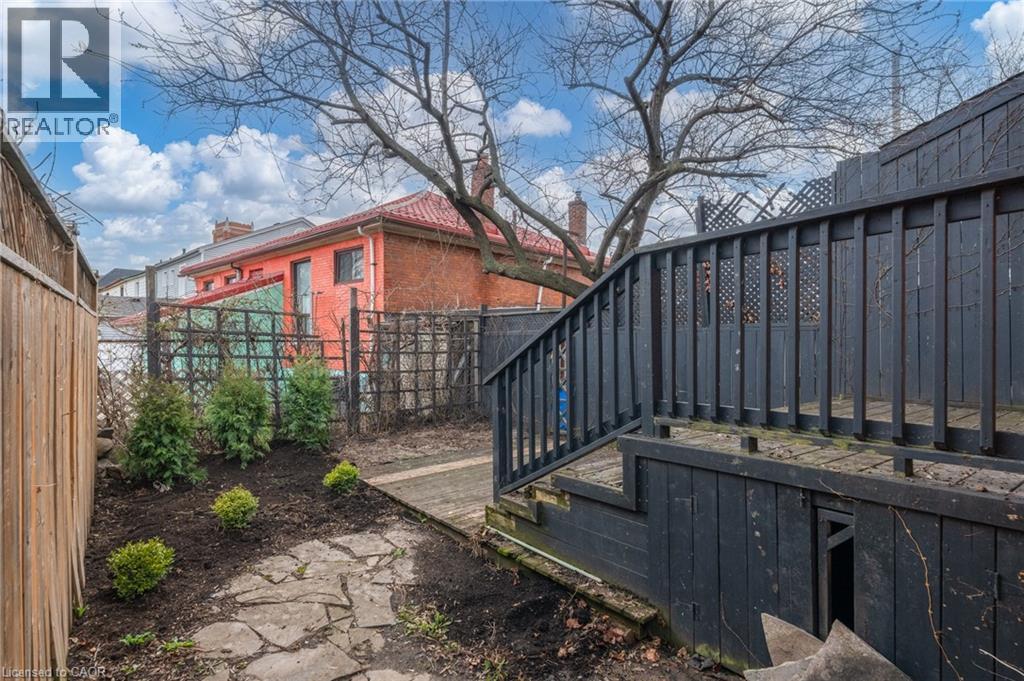 The property features a stone pathway, landscaping with young evergreen shrubs, and a dark-stained deck with railings - 198 Bay Street N, Hamilton, ON - Outdoor