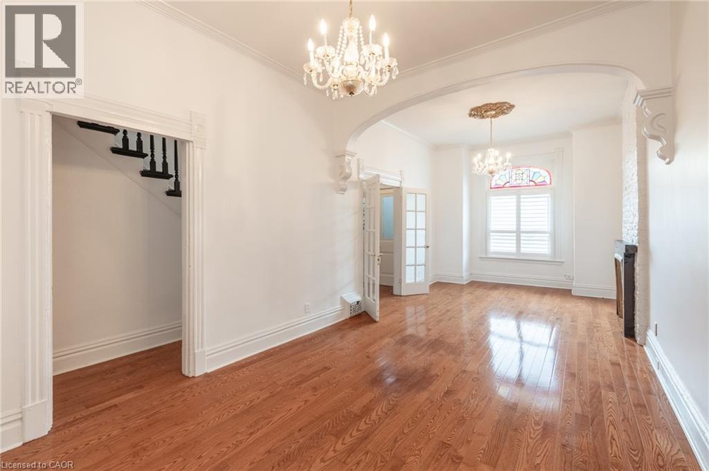 Spacious room featuring hardwood floors, a decorative chandelier, an arched doorway, and white window shutters - 198 Bay Street N, Hamilton, ON - Indoor Photo Showing Other Room