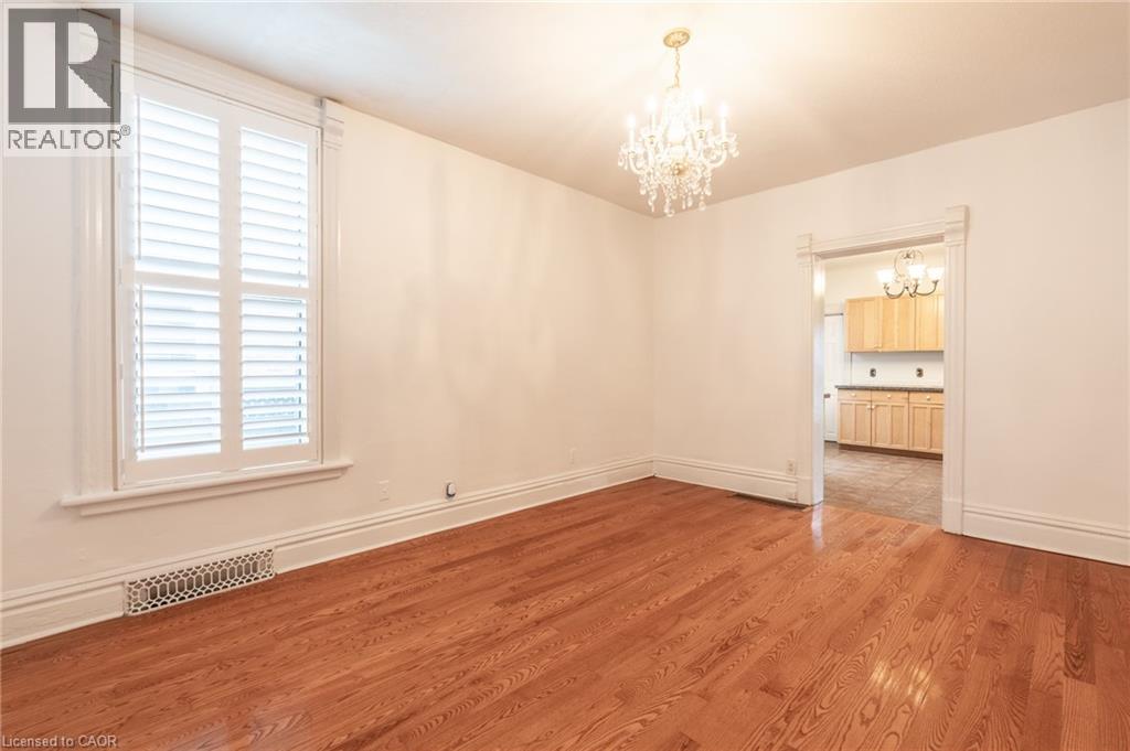This inviting space features lustrous hardwood floors, a prominent window with white plantation shutters, and an ornate chandelier providing elegant lighting - 198 Bay Street N, Hamilton, ON - Indoor Photo Showing Other Room