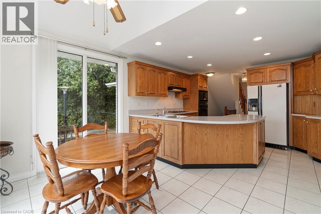 The kitchen features light wood cabinetry, a built-in oven, a refrigerator, and a curved island with a white countertop - 36 Buckingham Drive, Hamilton, ON - Indoor