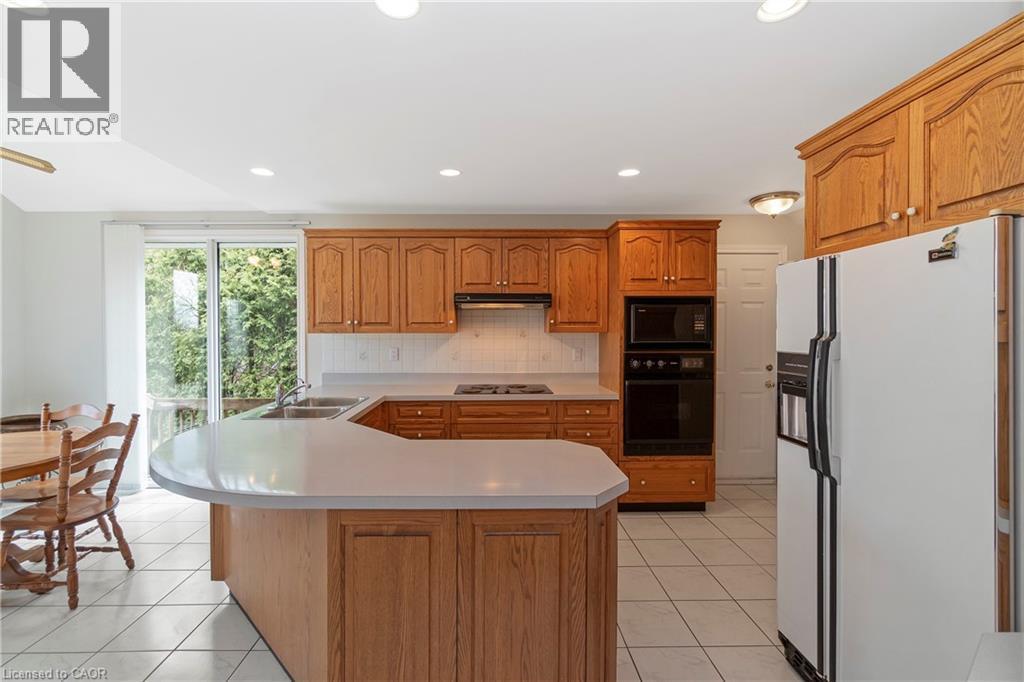 The kitchen features wood cabinetry, a built-in oven and microwave, a white refrigerator, and white tile flooring - 36 Buckingham Drive, Hamilton, ON - Indoor Photo Showing Kitchen With Double Sink