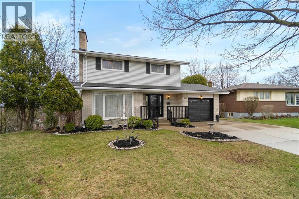 The property features a two-story design with a light-colored brick and siding exterior, a dark gray garage door, and a paved driveway - 36 Buckingham Drive, Hamilton, ON - Outdoor With Facade